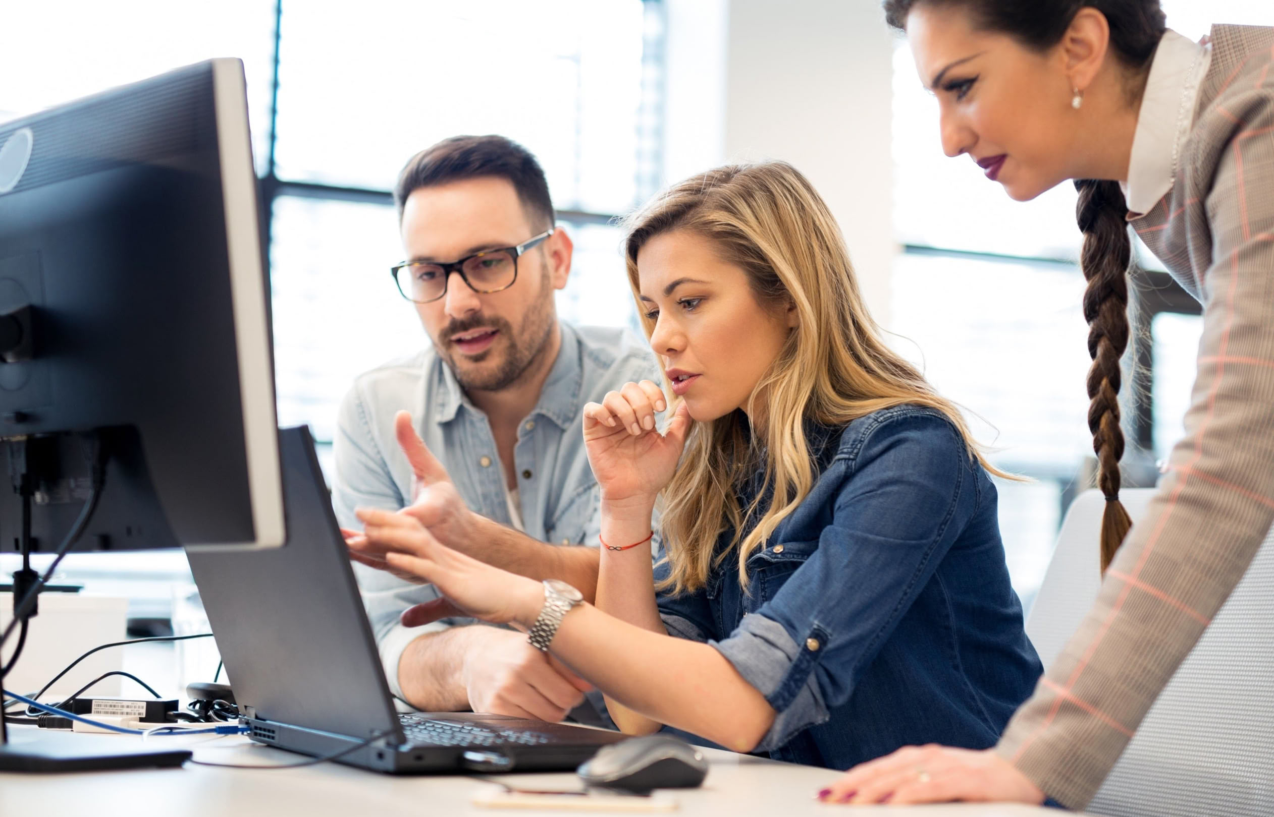 Drei Personen arbeiten gemeinsam an einem Computerbildschirm in einem Büro.